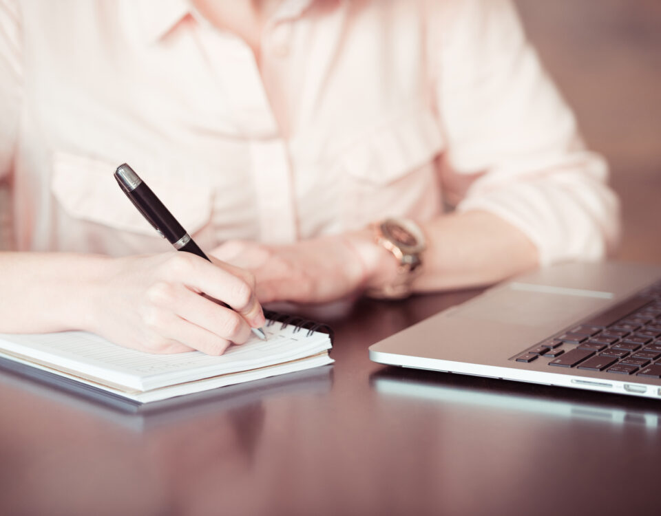 Building Gender Discrimination Case: a woman writes in a notebook while sitting in front of a computer.